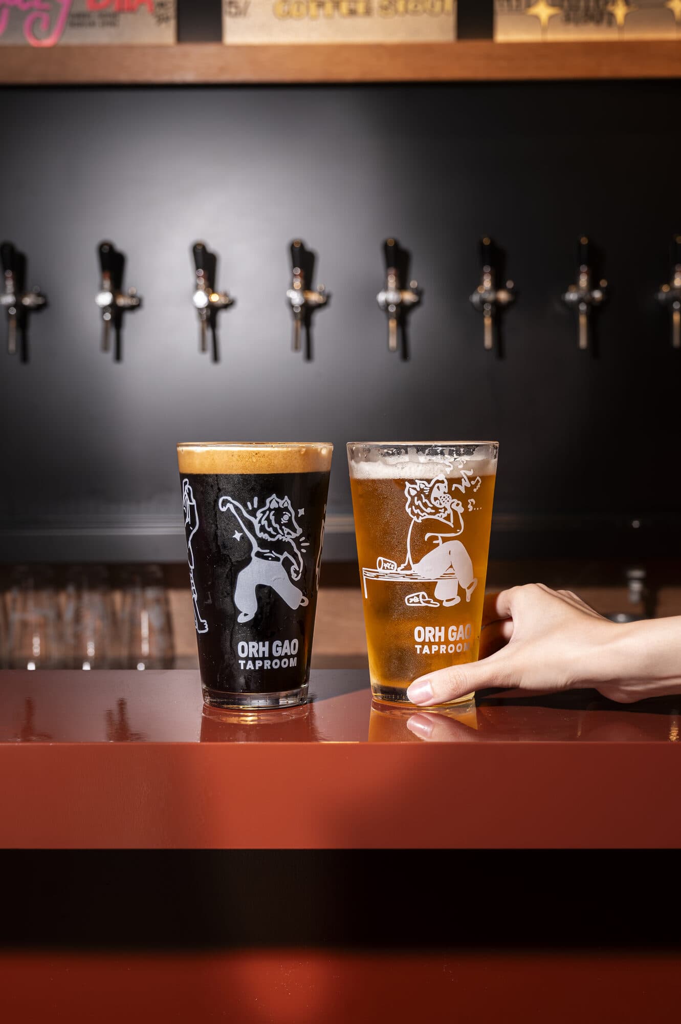 Two branded Orh Gao Taproom beer glasses on a bar counter, with a row of beer taps on the wall behind