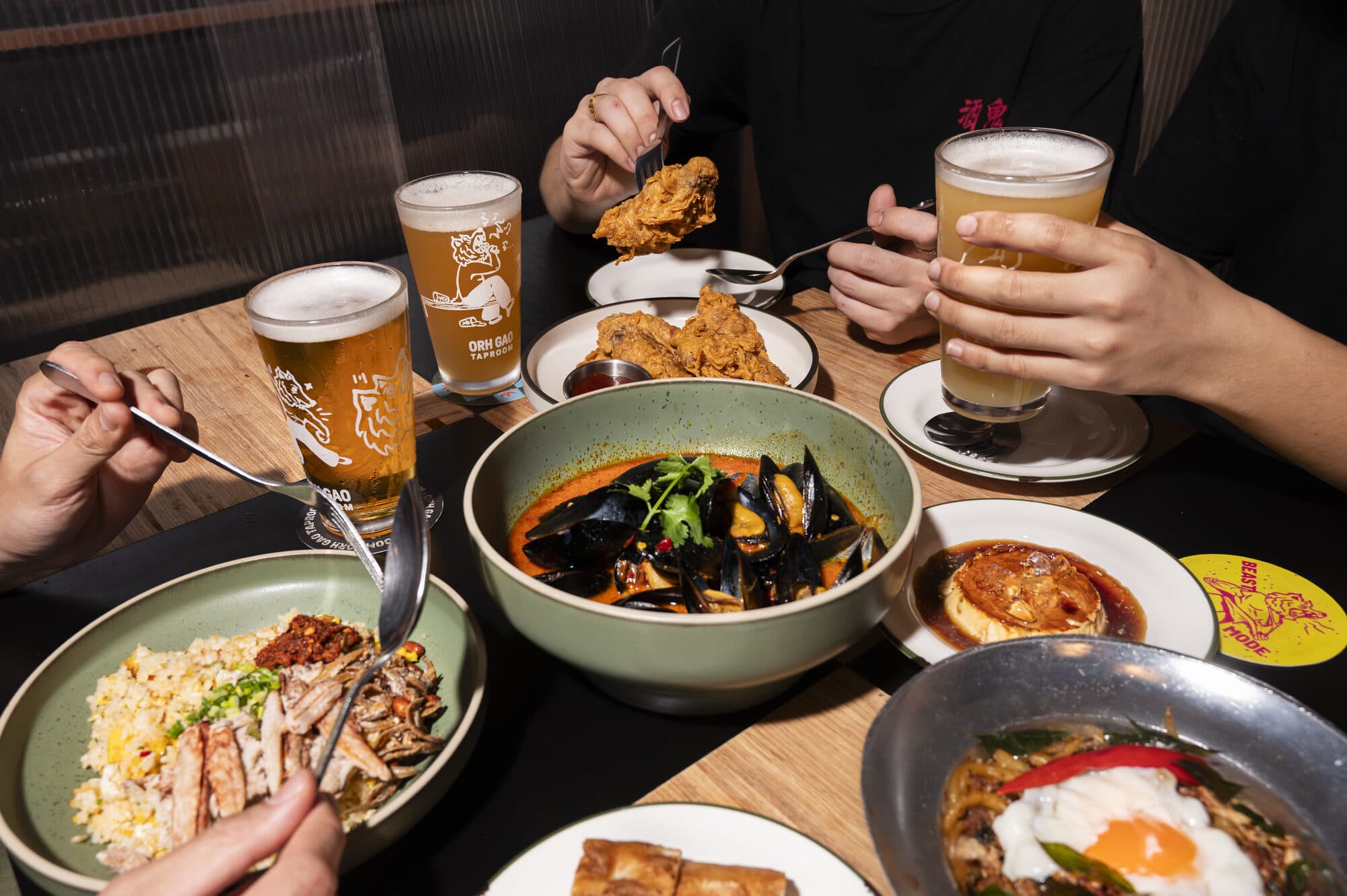 Diners serving themselves from shared bowls of noodles, curry and rice at a table set with glasses of beer