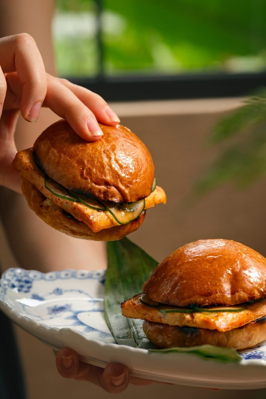 Otak-otak sliders in brioche buns held above a porcelain plate at Tembusu