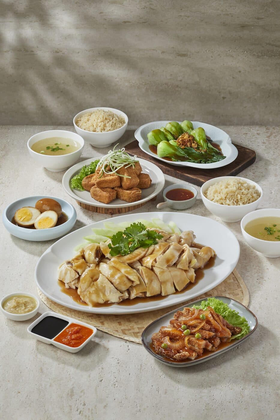 Table spread of poached chicken, chicken rice, soup, braised egg and side dishes