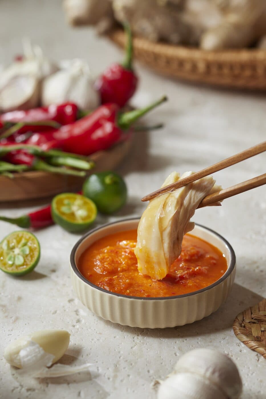 Piece of poached chicken being dipped into a bowl of chilli sauce