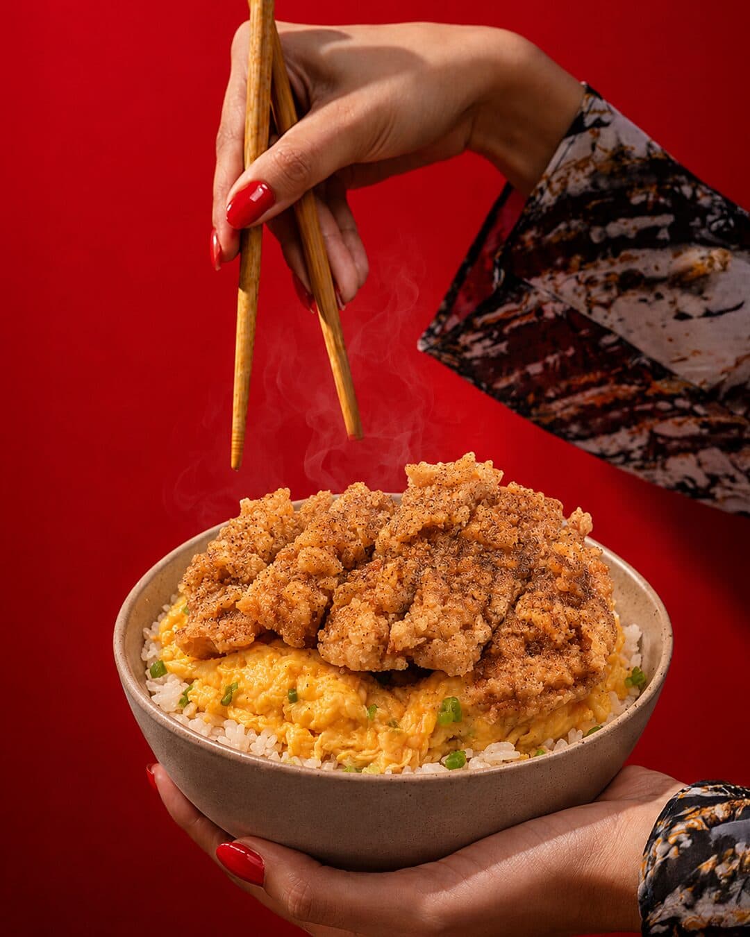 Hand holding a bowl of rice topped with a fried cutlet