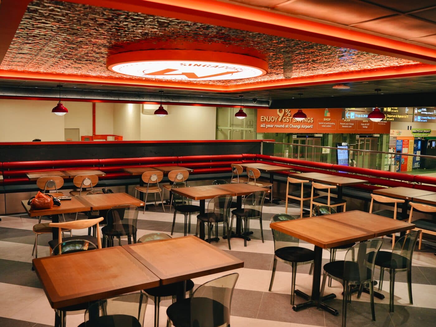 Dining area with timber tables, red pendant lamps and a circular illuminated ceiling sign