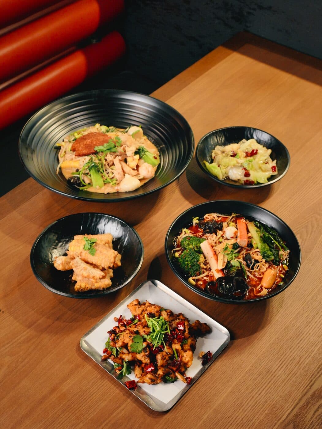 Four bowls of mala dishes and sides arranged on a timber table