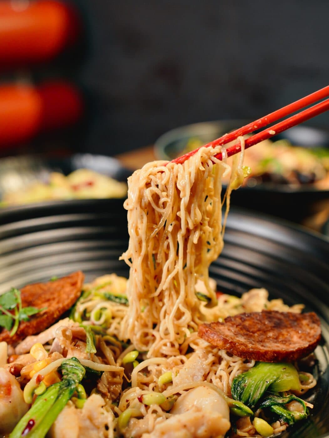 Chopsticks lifting noodles topped with sliced meat from a dark bowl
