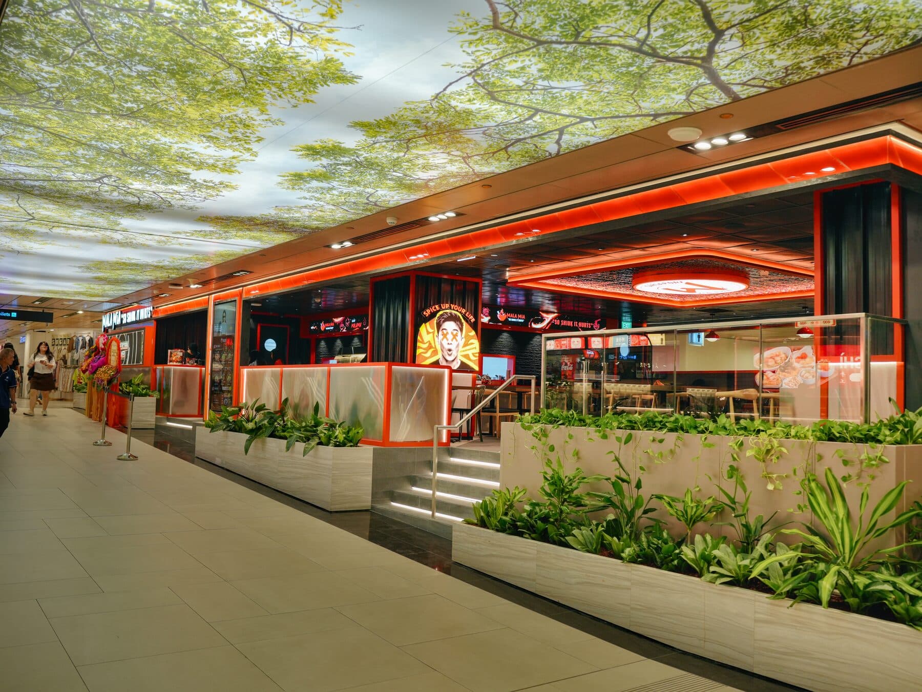 Mala Mia shopfront at Changi Airport Terminal 3 basement two, with red signage reading “so shiok it hurts” and planters along the walkway